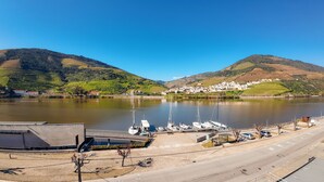A marina with boats docked, a road in the foreground, and a town with buildings on the hills in the background. - Hotel Folgosa Douro (Armamar)