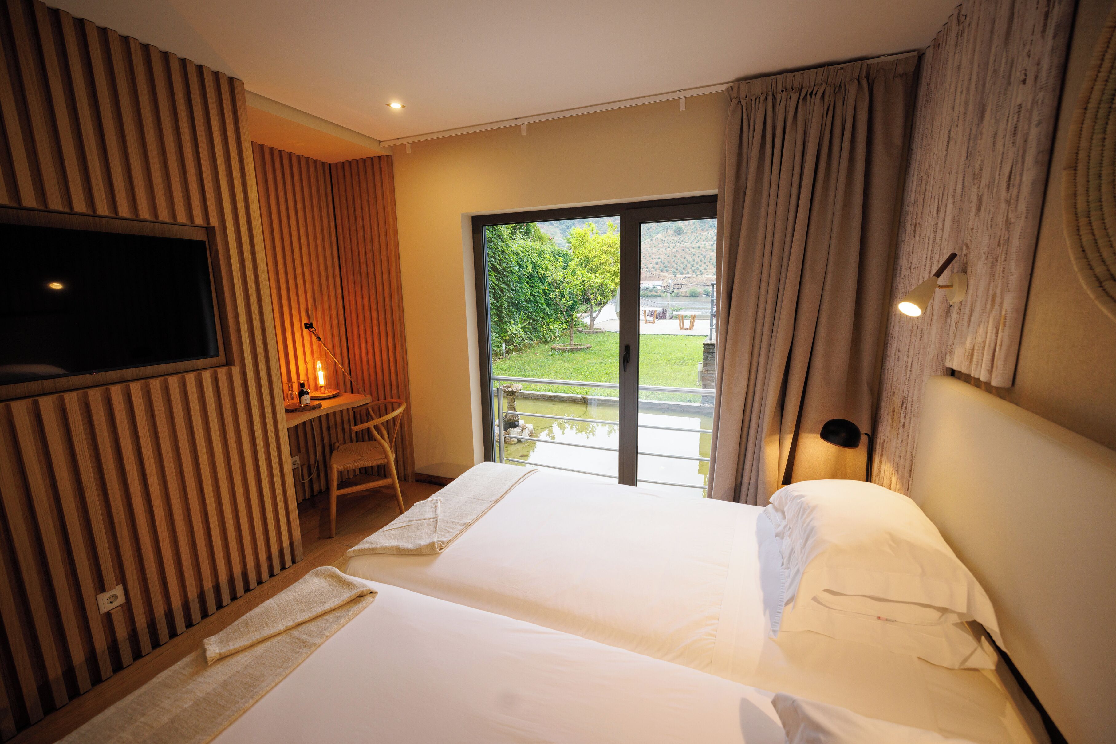 Habitación de hotel con una cama grande, televisor en la pared, escritorio con silla y vistas al exterior a través de una puerta corrediza de cristal.