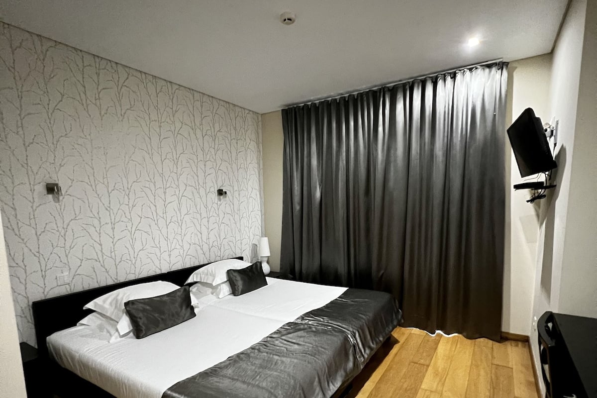 A hotel room with a bed, a desk, a TV, and a window with curtains.