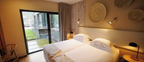 A hotel room with a large bed, a chair, a nightstand, and a view of the outside.