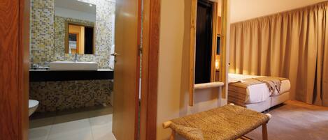 A hotel room with a bathroom, a bed, and a bench.