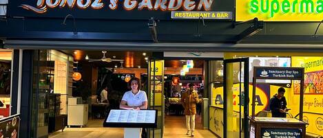 A beach hotel named 'Tonoz's Garden' with a restaurant and bar, and a supermarket sign.