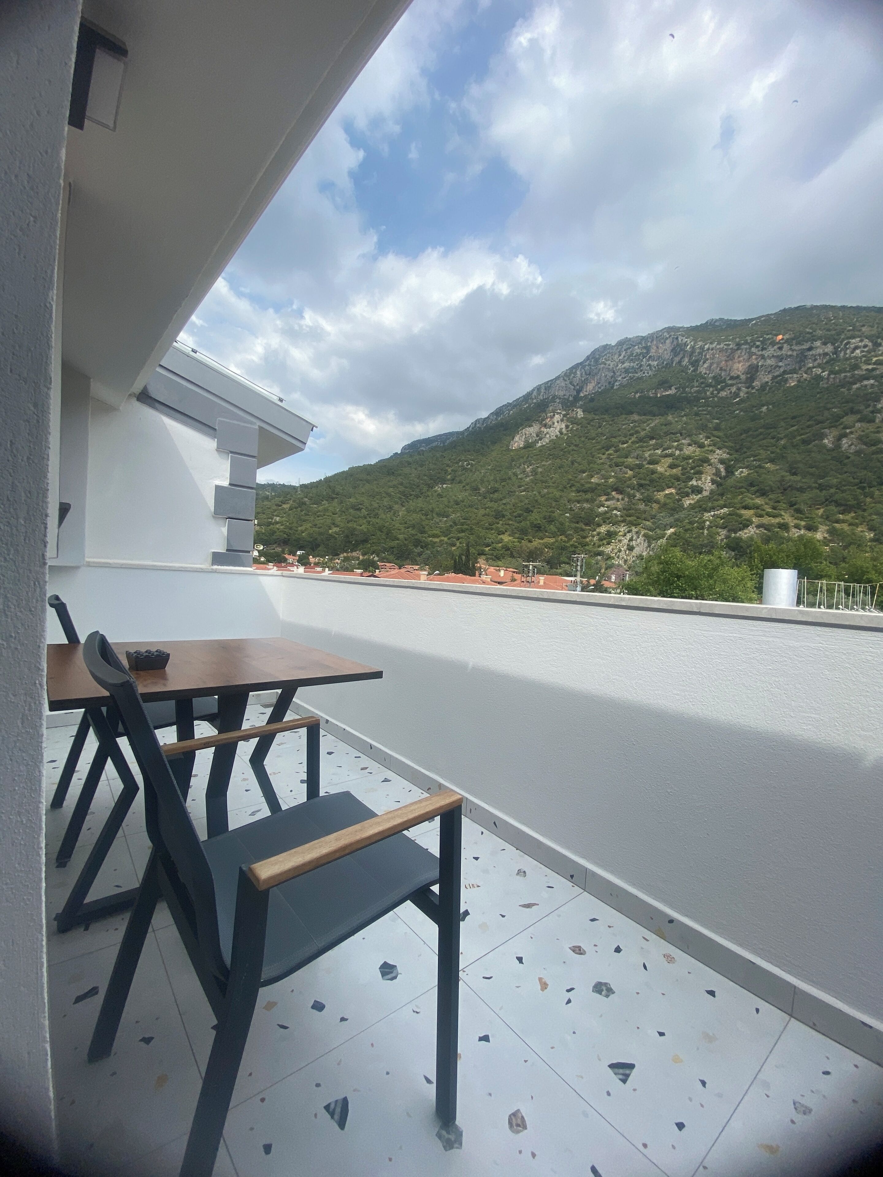 A terrace with a table and chairs, overlooking a mountain and a coastal area.