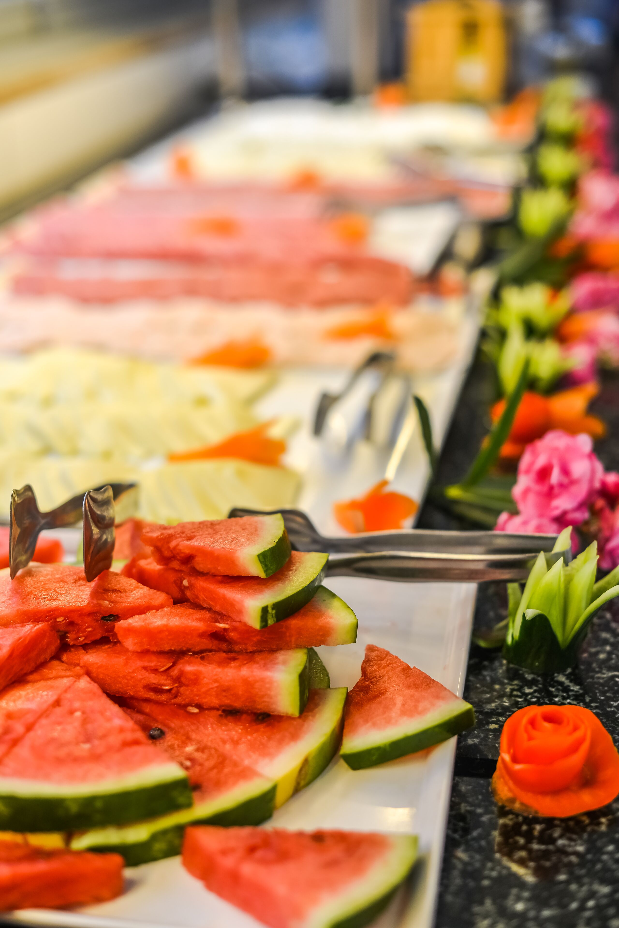 A buffet with various food items including watermelon slices and a rose-shaped dessert.