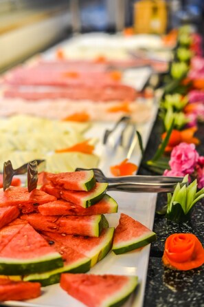 Un bufé con diversos alimentos, incluyendo rebanadas de sandía y un postre con forma de rosa.
