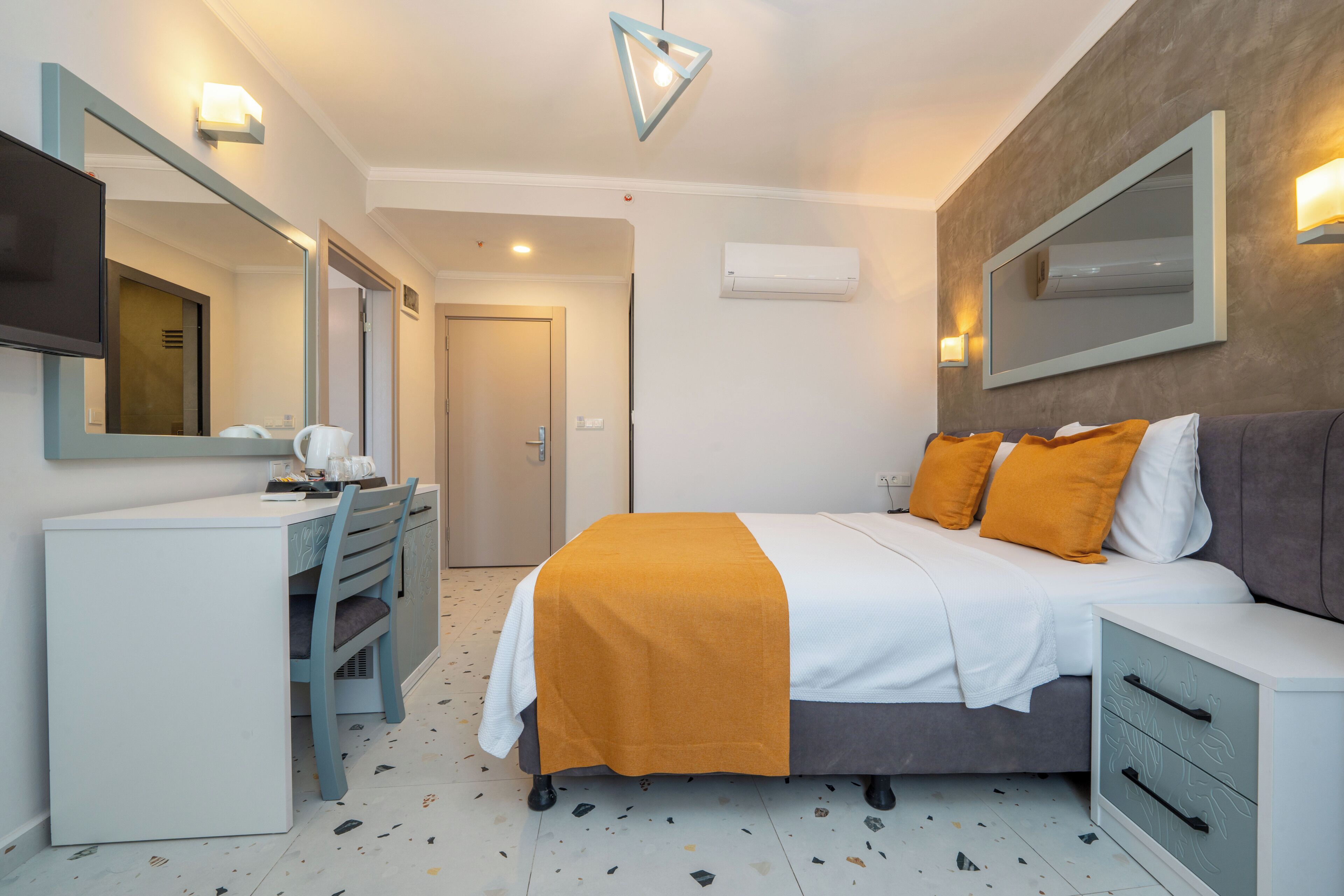 A hotel room with a bed, bedside table, desk, chair, and a large mirror.