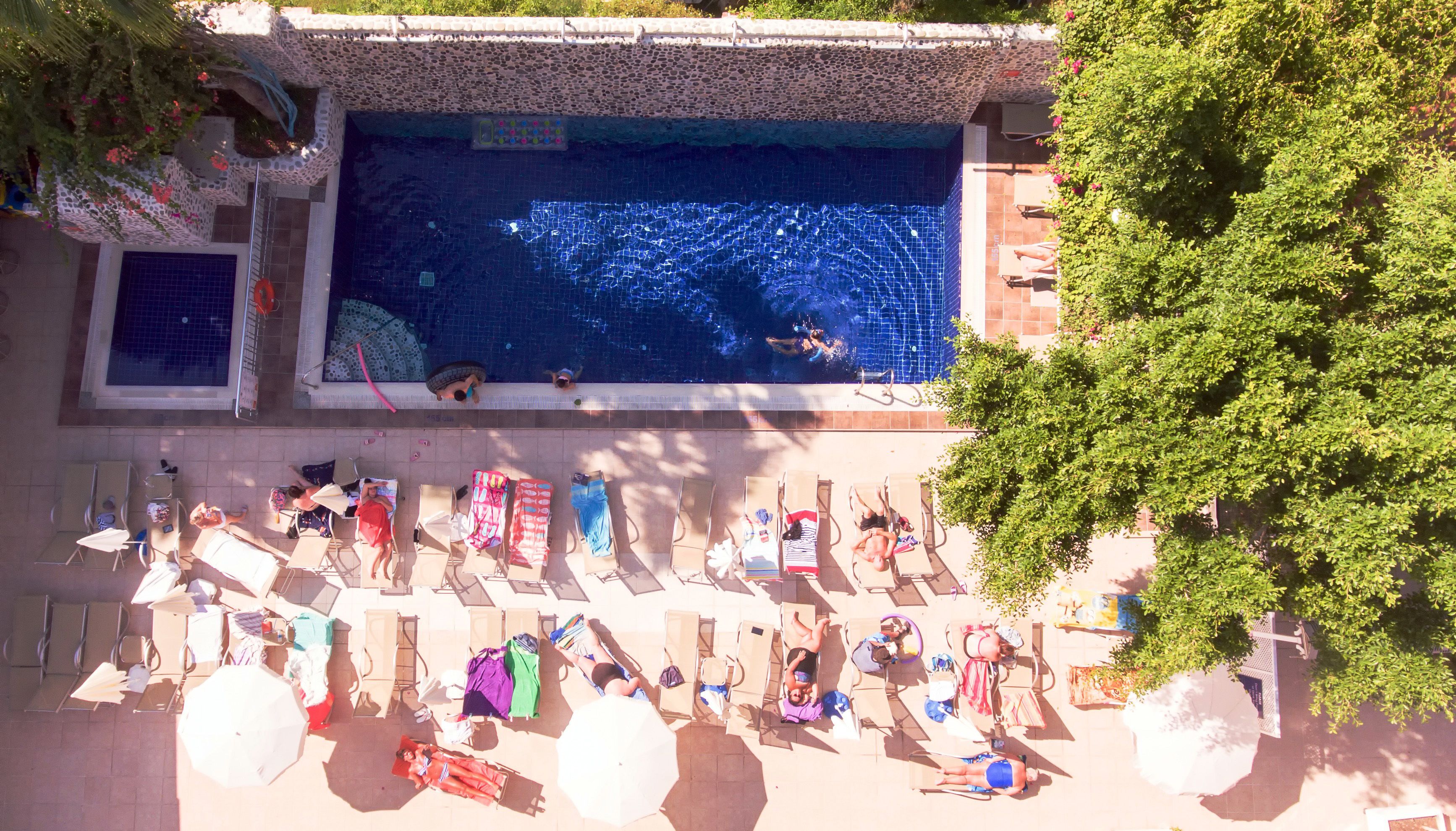 A rooftop pool with a tiled floor, surrounded by lounge chairs and umbrellas.