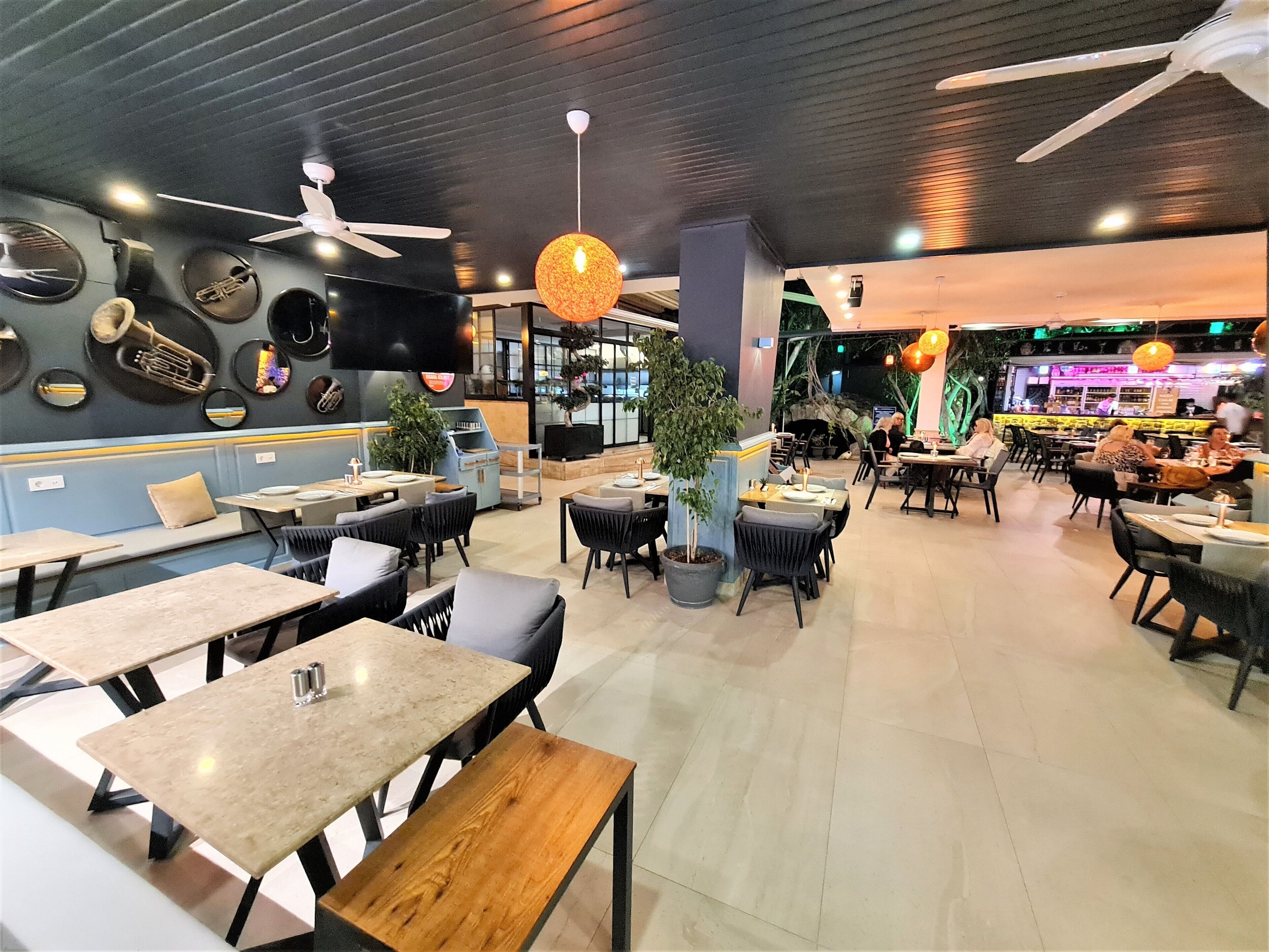 Interior de restaurante con varias mesas y sillas, ventiladores de techo y elementos decorativos en las paredes.