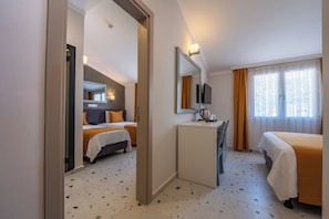 Habitación de hotel con dos camas, un escritorio, un espejo, un televisor y una ventana con cortinas.