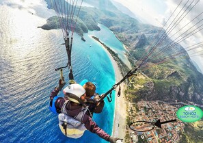 Un parapentista sobre una zona costera con playa y pueblo abajo.