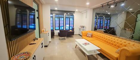 A modern living room with a large flat-screen TV, a sofa, a coffee table, and a dining area with a table and chairs.
