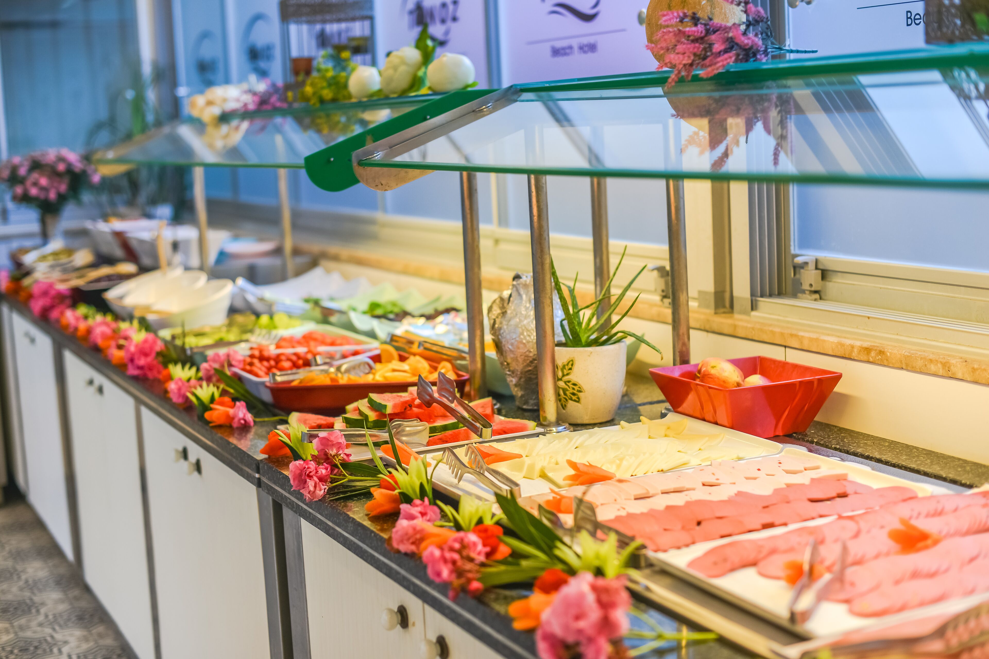 A buffet with various food items and decorative flowers.