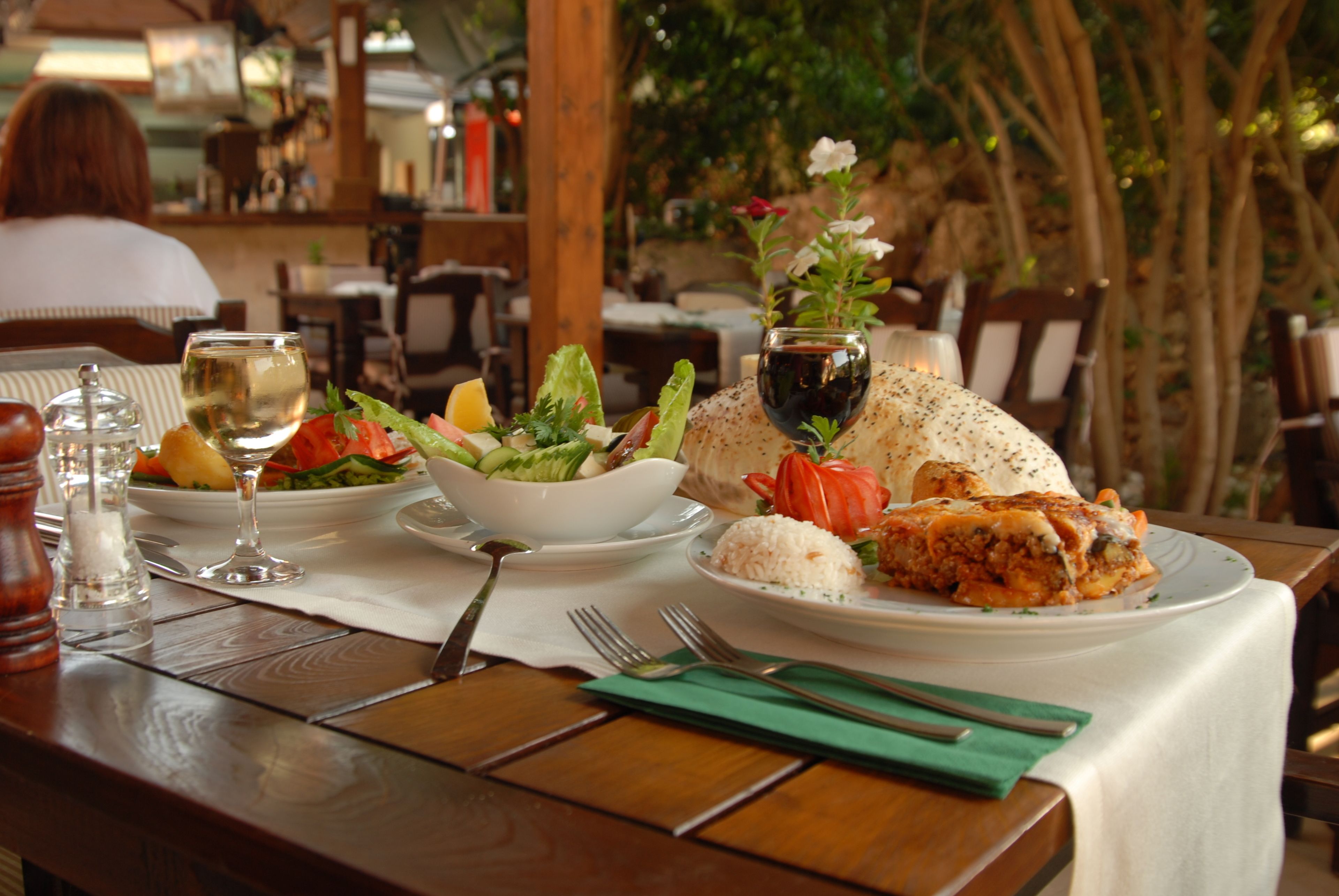 A dining table with a meal consisting of rice, salad, and a main dish, set in an outdoor dining area with wooden furniture and a view of trees.