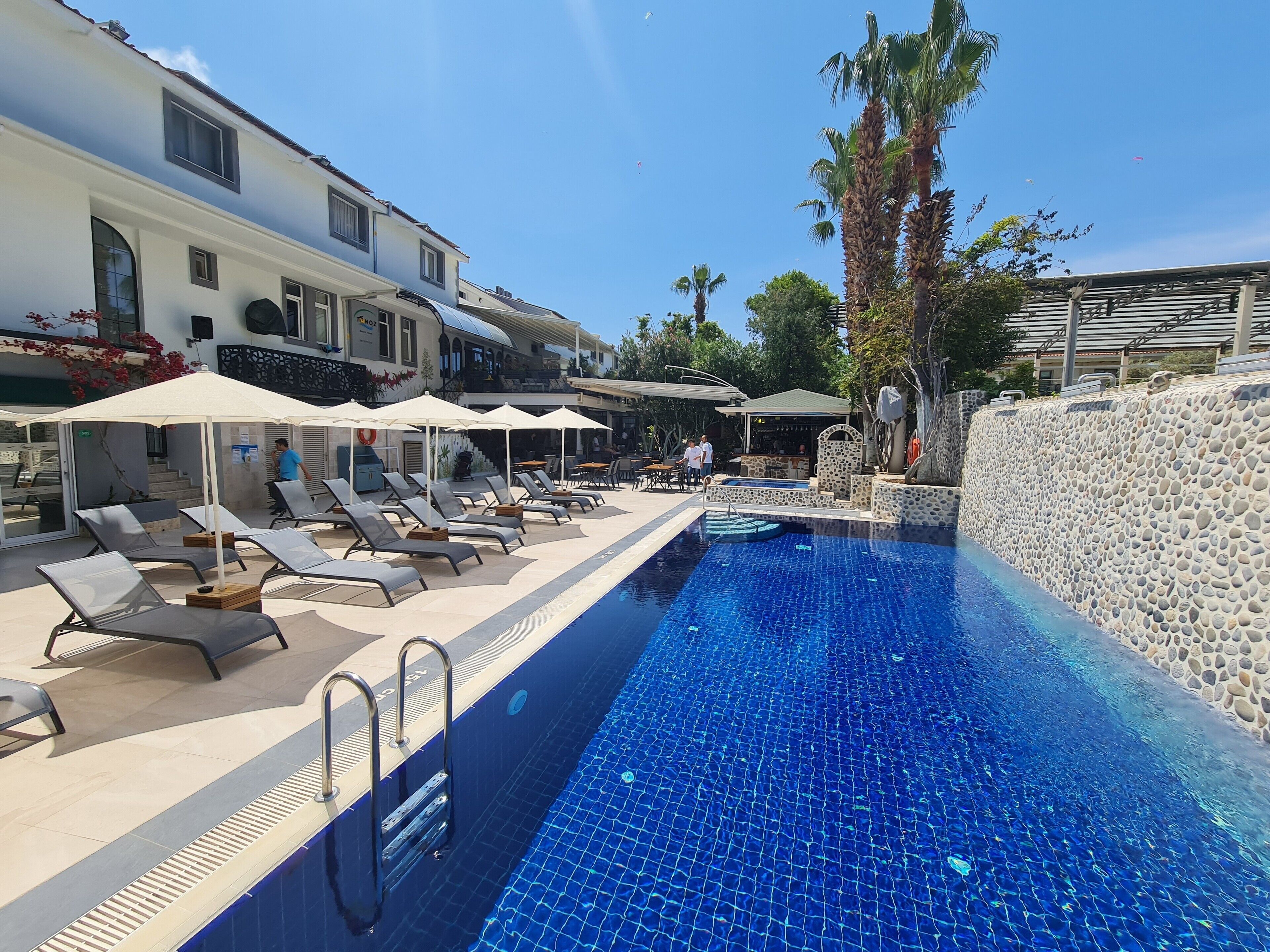 A pool area with lounge chairs and umbrellas, a stone wall, and a bar area.