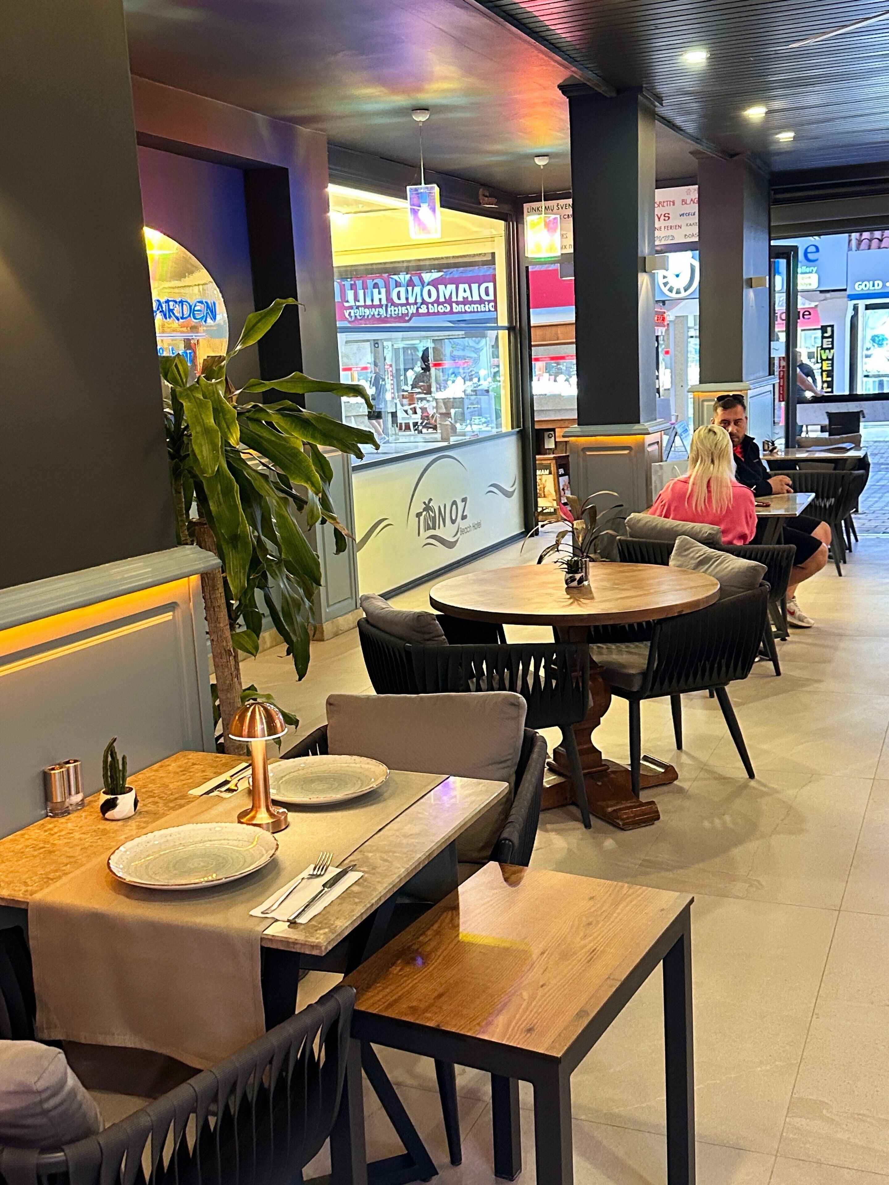 Interno di un ristorante con tavoli e sedie rotonde, una pianta in vaso e un bancone con il menu.