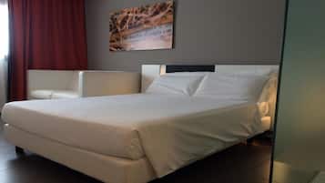 Ein modernes Hotelzimmer mit einem großen Bett, einem weißen Sessel und einem Wandbild.