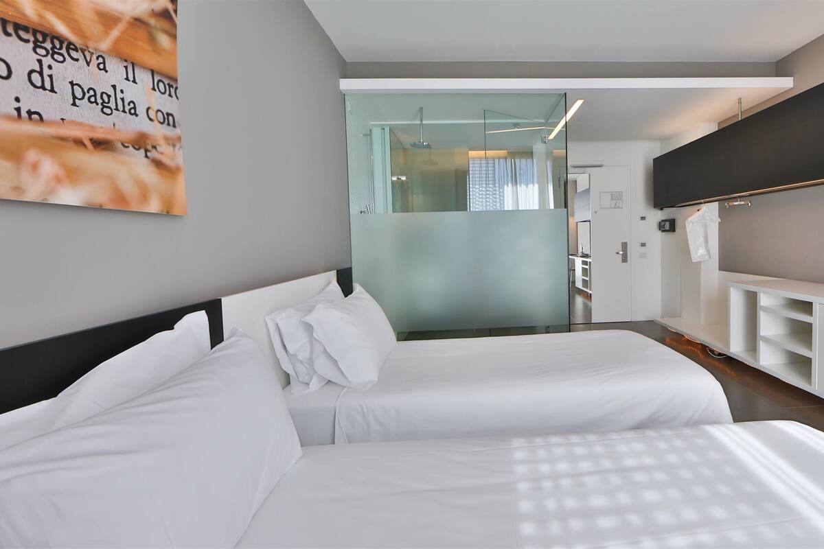 A modern hotel room with a large bed, a built-in TV, and a glass shower area.