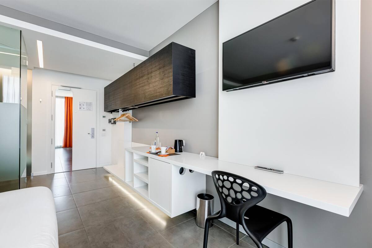 A modern hotel room with a large bed, a desk with a chair, a flat-screen TV, and a wardrobe.