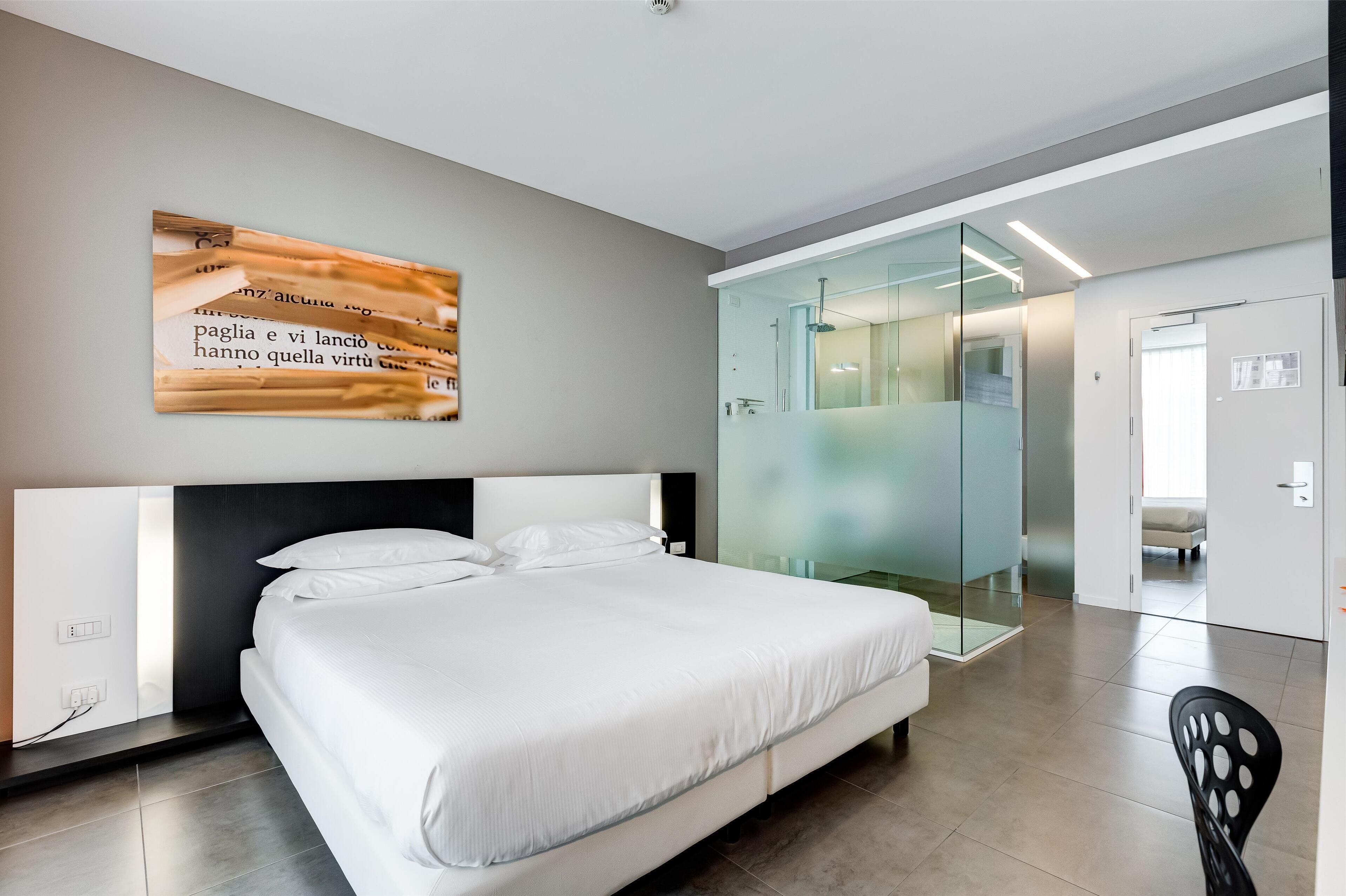 A modern hotel room with a large bed, a glass shower enclosure, and a wall-mounted artwork.