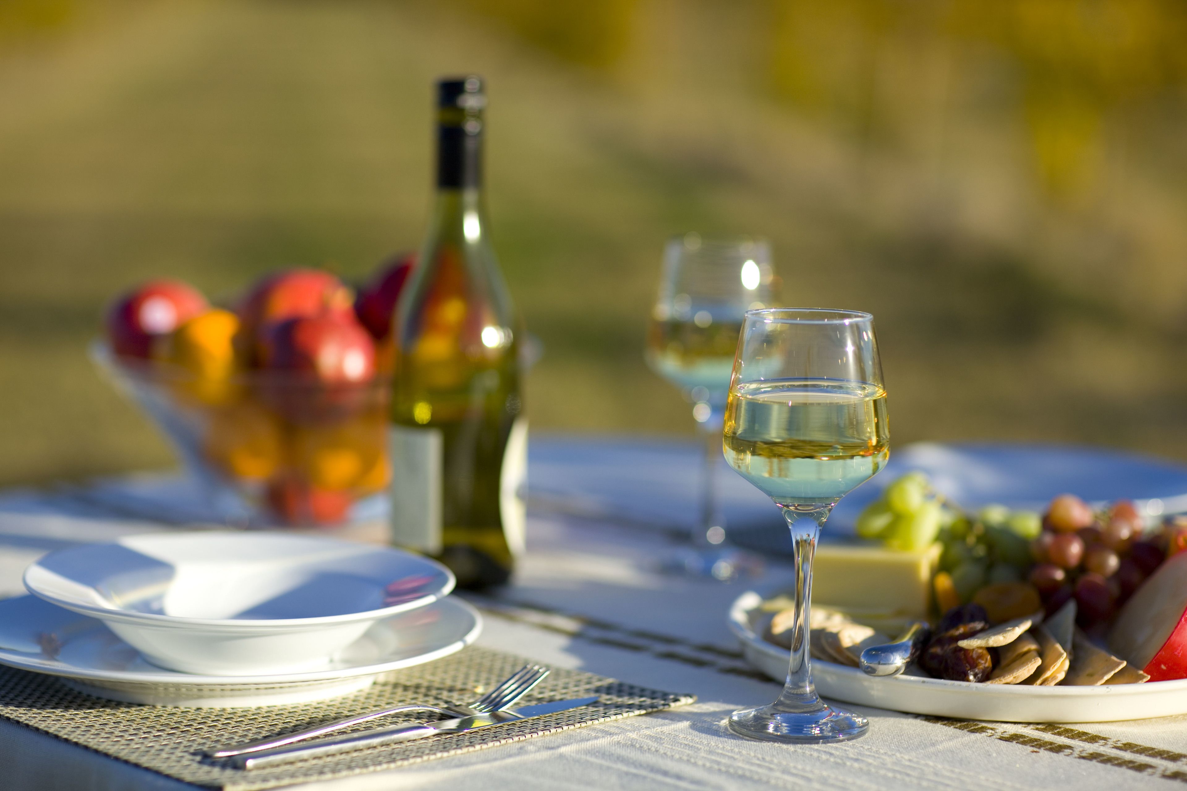 A table set with a wine bottle, glasses, a bowl of fruit, and a plate of cheese and crackers.