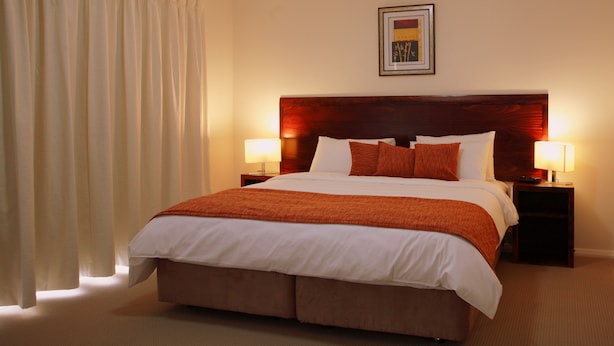 A hotel room with a large bed, two bedside tables with lamps, a headboard, and a framed picture on the wall. - Talga Estate (Lovedale)