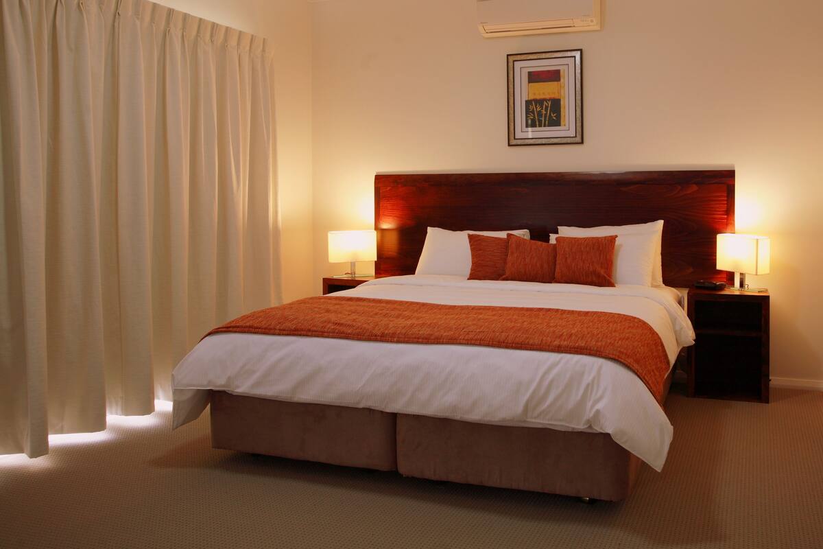 A hotel room with a large bed, two bedside tables with lamps, a headboard, and a framed picture on the wall.
