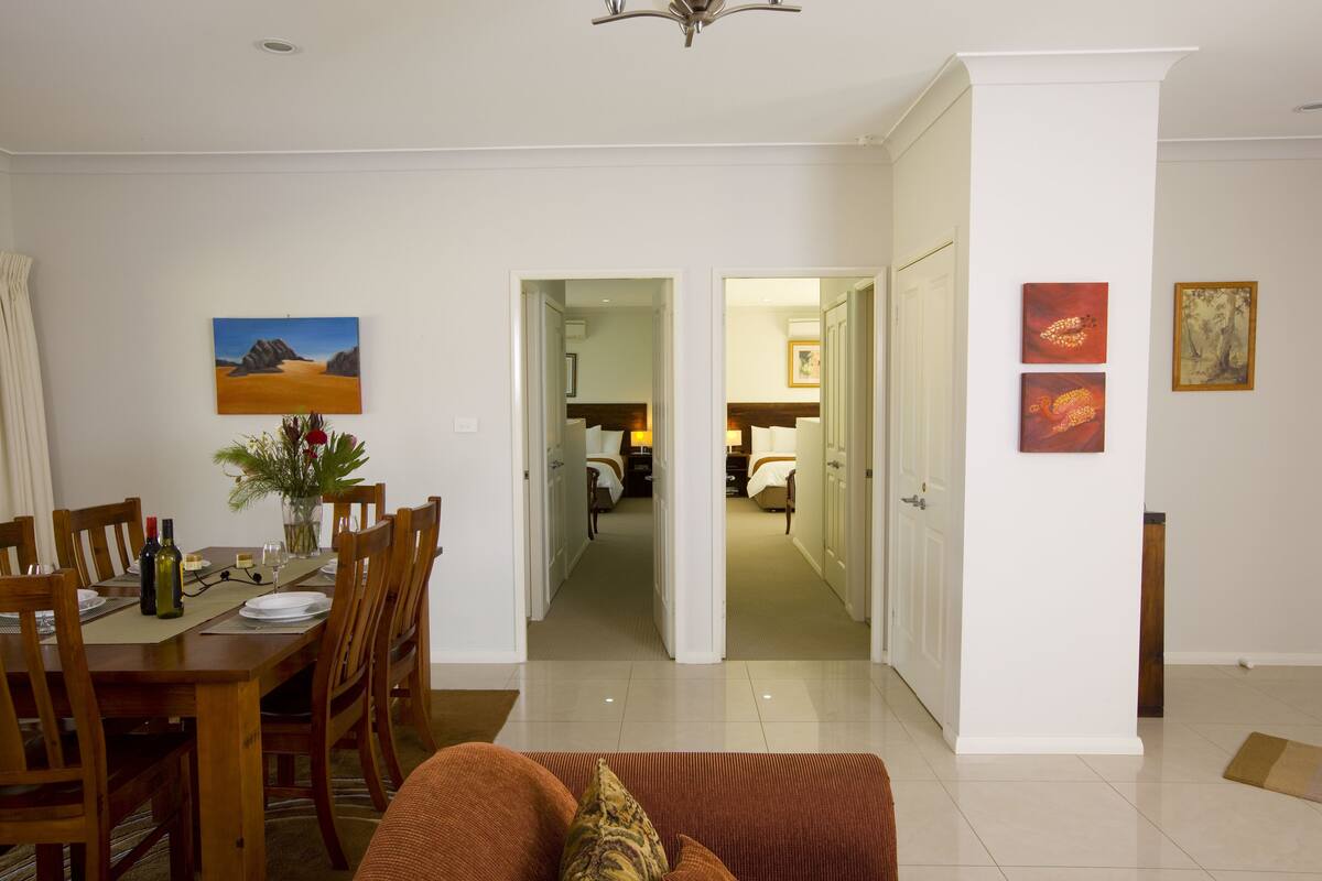 A dining area with a wooden table set for four, a vase with flowers, and a painting on the wall.