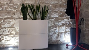 Una habitación con pared de piedra, un mueble blanco para guardar objetos y un perchero rojo con un paraguas negro.