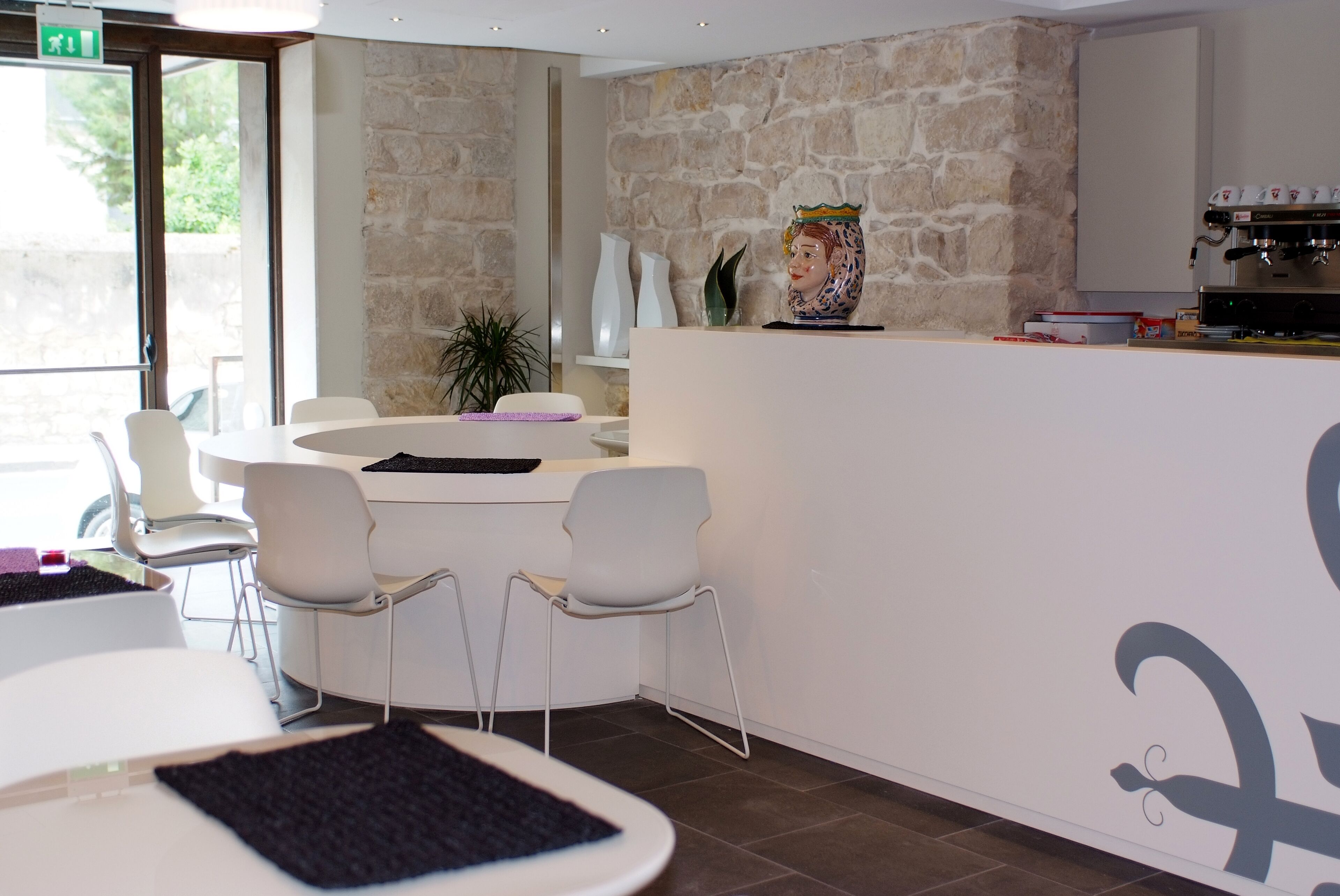 Un moderno vestíbulo de hotel con una pared de piedra, una recepción, sillas blancas y una máquina de café.