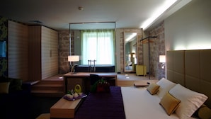 Habitación de hotel con cama, escritorio, espejo, armario y baño visible a través de una puerta abierta.
