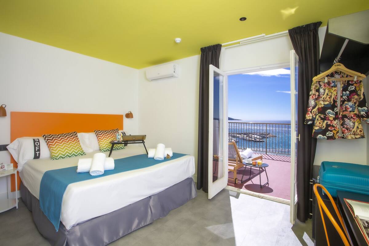 A hotel room with a bed, a balcony with a view, and a hanging garment rack.