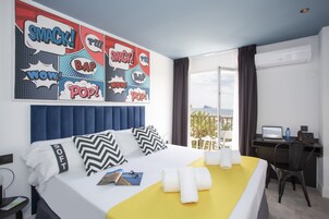 A hotel room with a bed, a desk with a laptop, and a view of the sea.
