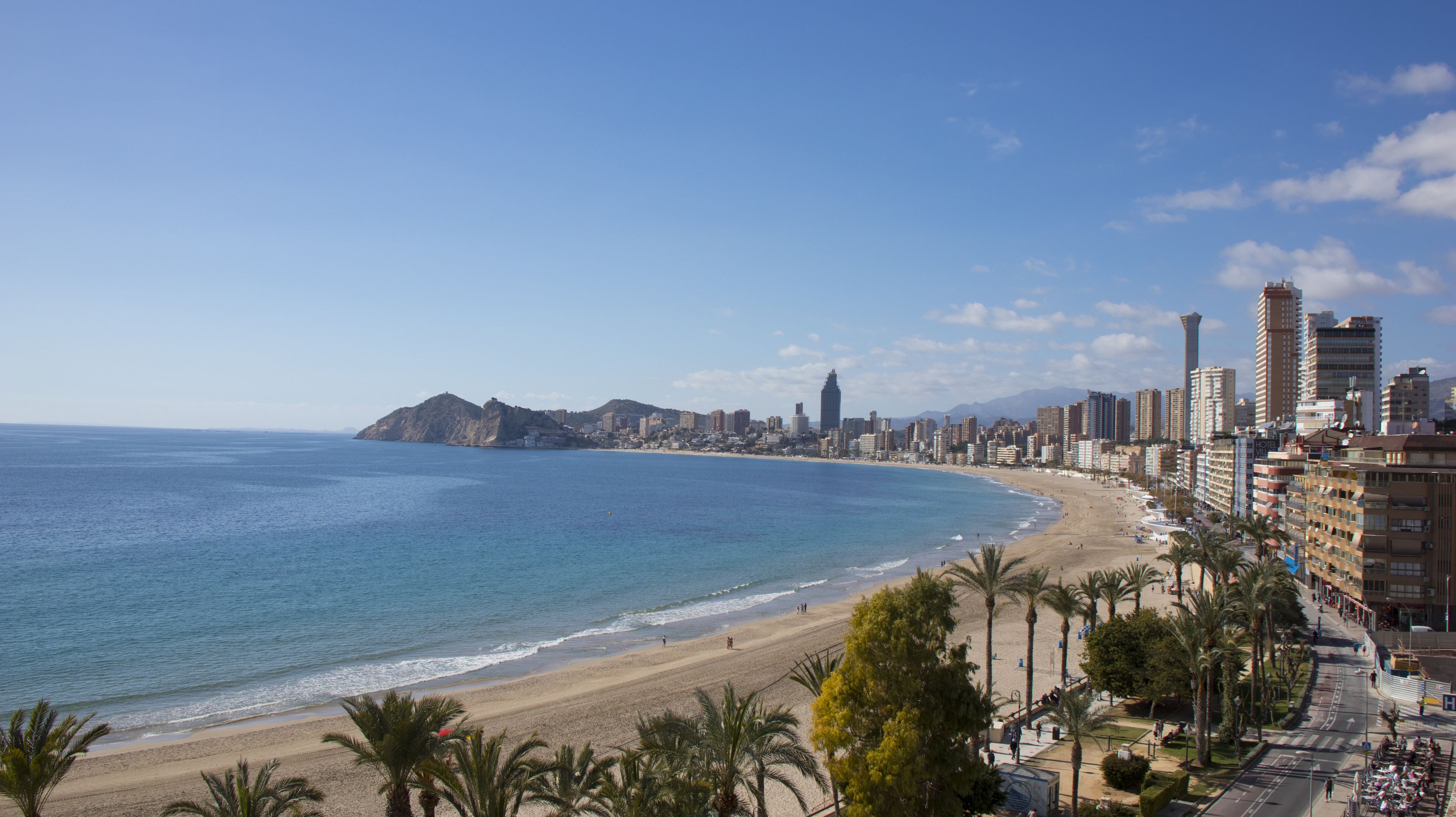 Un paysage urbain côtier avec une plage, des immeubles de grande hauteur et une montagne imposante qui se profile à l’horizon.