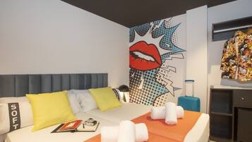 Una camera d'albergo con un letto, cuscini, un'opera d'arte a parete, una valigia e un armadio.