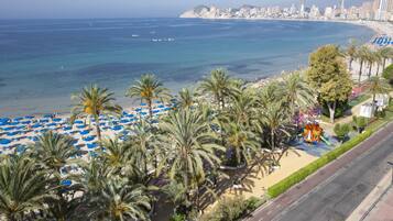 Una playa con palmeras, una carretera y un paisaje urbano al fondo.