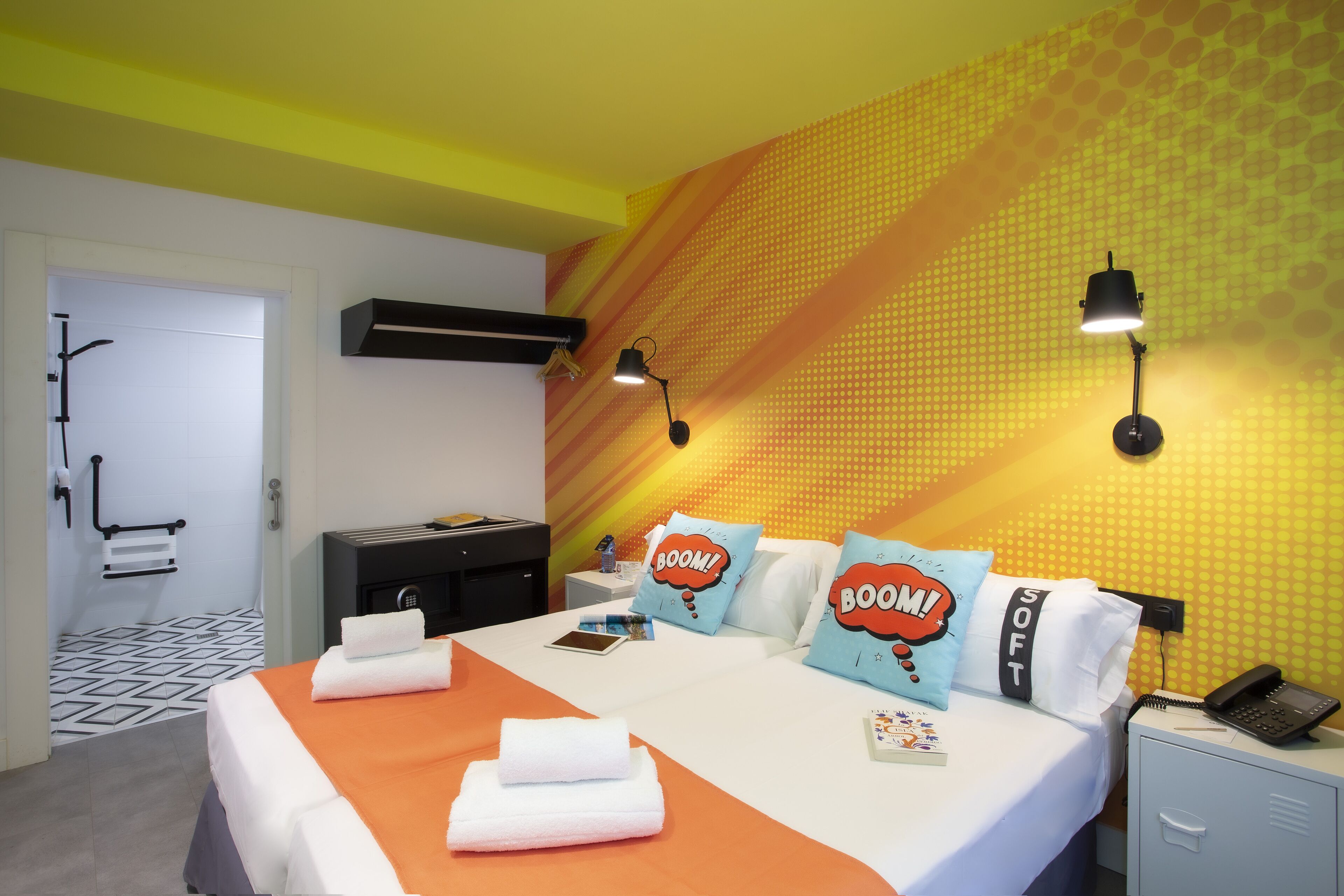 Une chambre d’hôtel avec un lit, des oreillers, une table de chevet, un téléphone et un mur orné d’un motif géométrique.