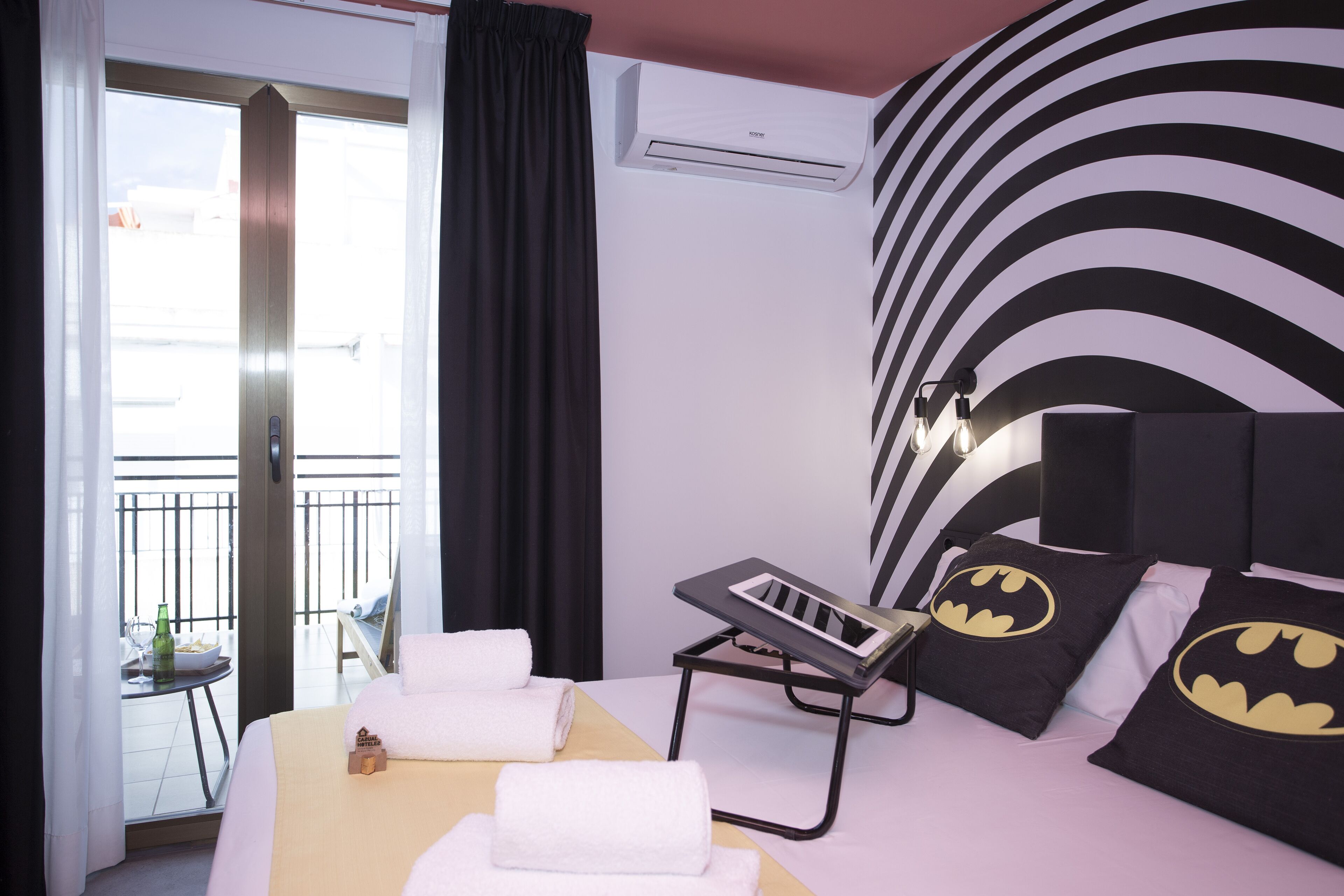 Una habitación de hotel con cama, mesita de noche, ventana y cortina.