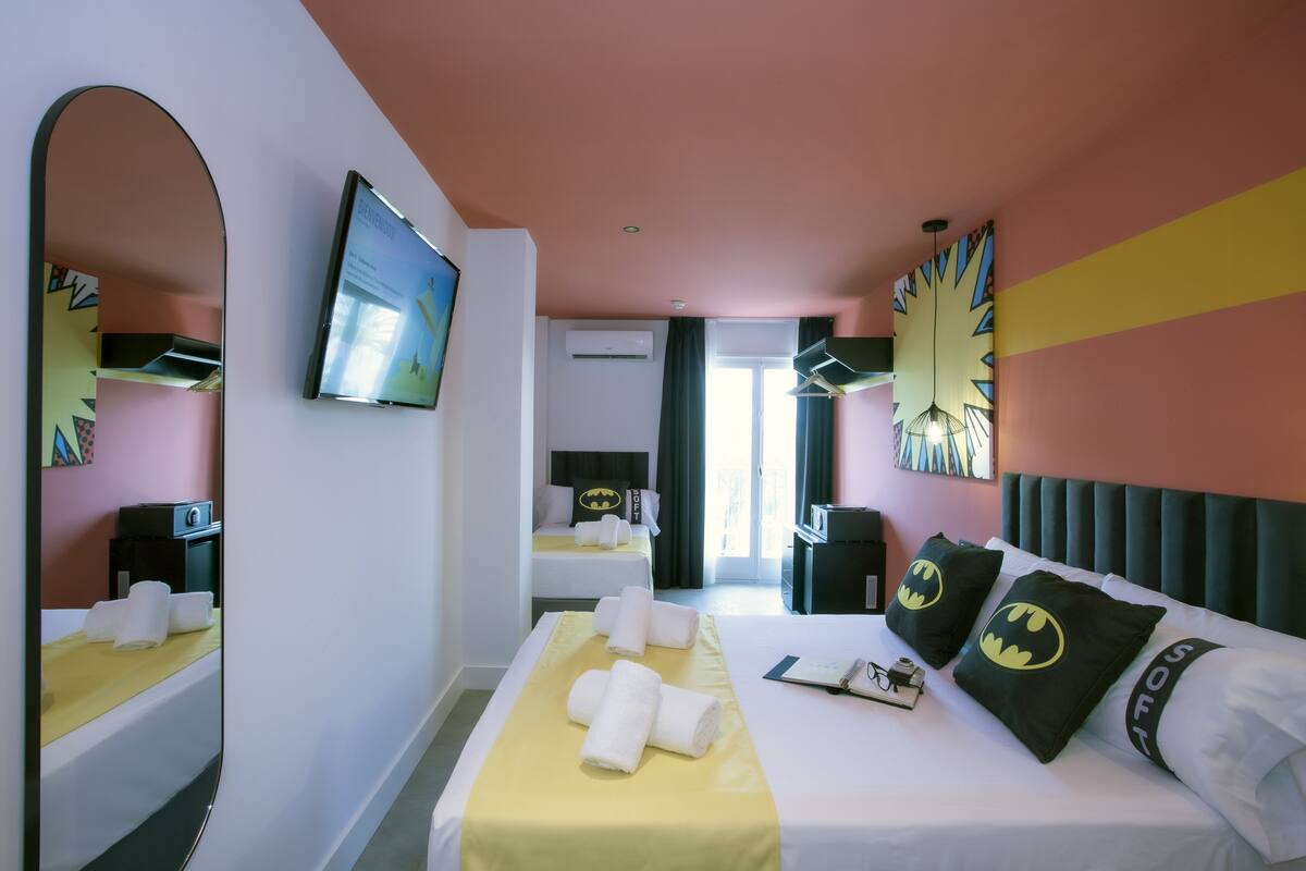 A hotel room with a bed, a TV, a mirror, and a window.