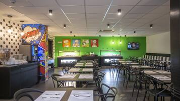 A restaurant with a green wall, a counter with a digital menu, and multiple tables with chairs.