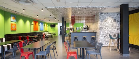 Un restaurante moderno con paredes verdes, varias mesas y sillas para comer, y una zona de bar.