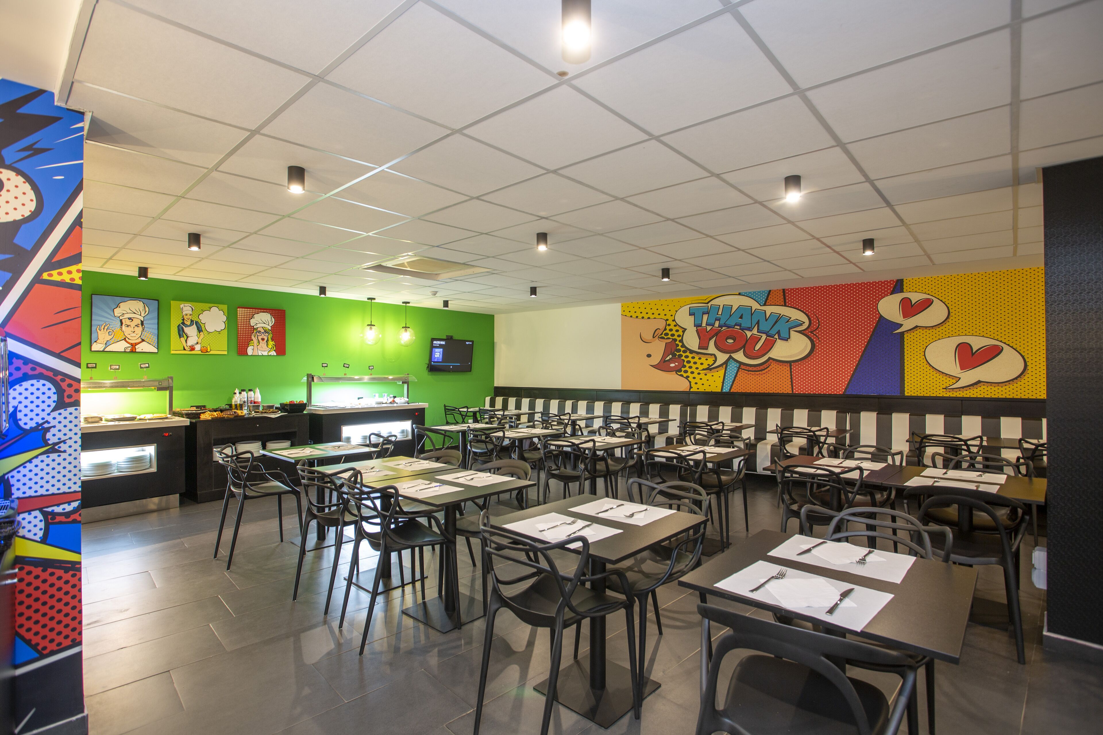 Un restaurante de colores brillantes con paredes verdes, murales con temática de dibujos animados y varias mesas y sillas.