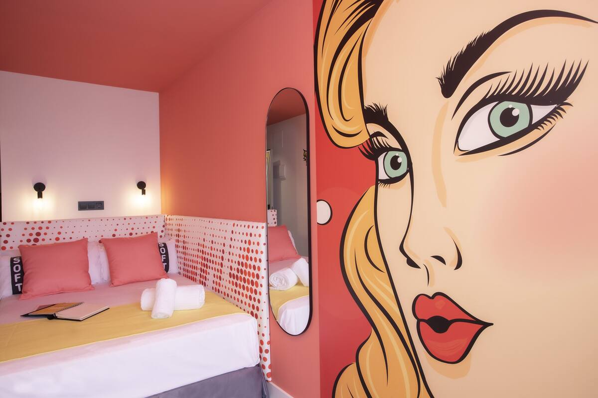 A hotel room with a bed, pillows, a mirror, and a wall mural.
