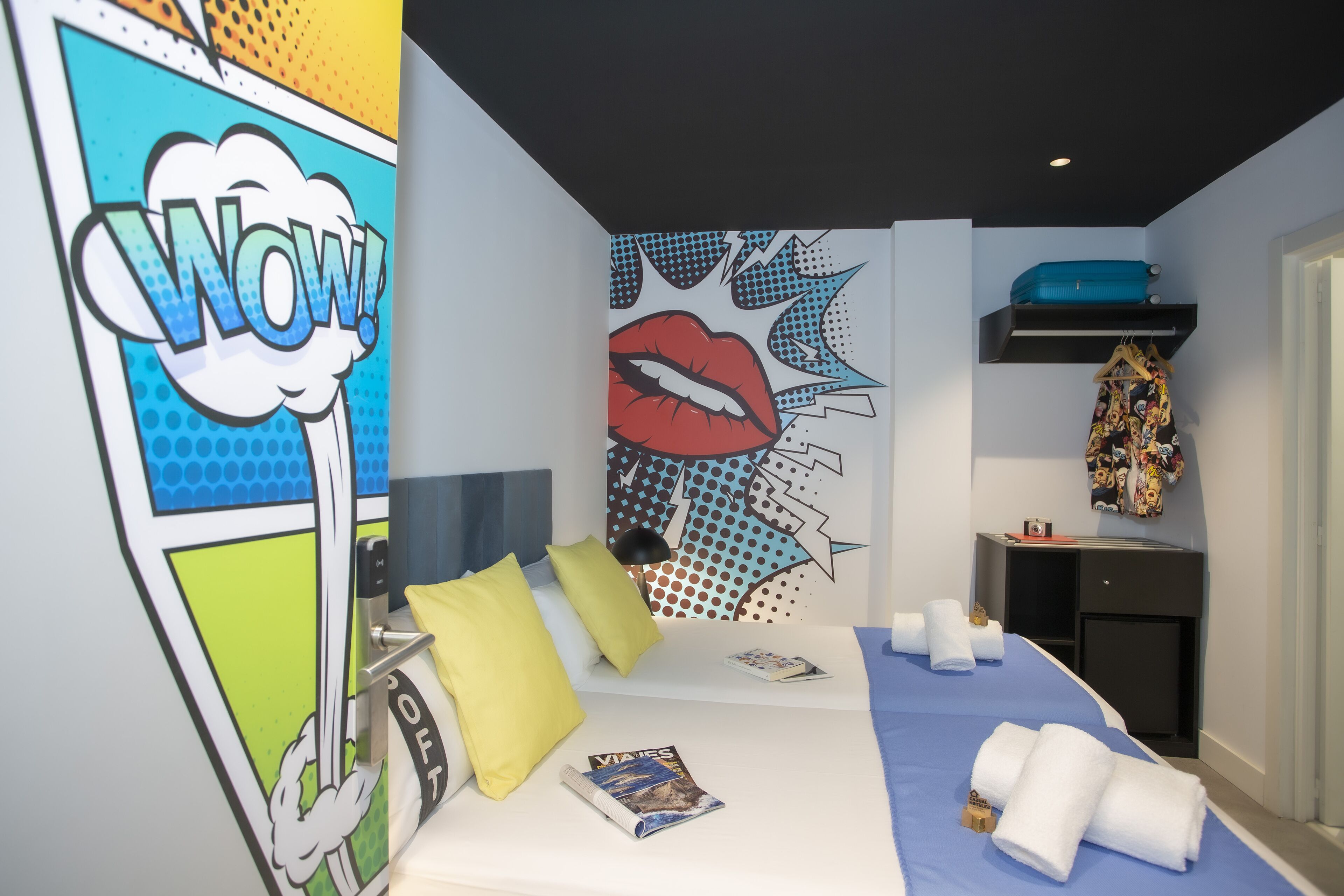 Una habitación de hotel moderna con cama, almohadas, una obra de arte en la pared, un escritorio y una estantería.