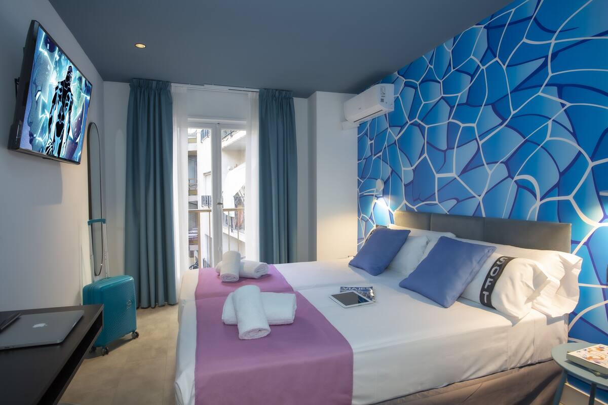 A hotel room with a bed, a TV, a suitcase, and a view of the outside.