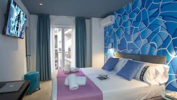 Habitación de hotel con cama, televisor, maleta y vistas al exterior.