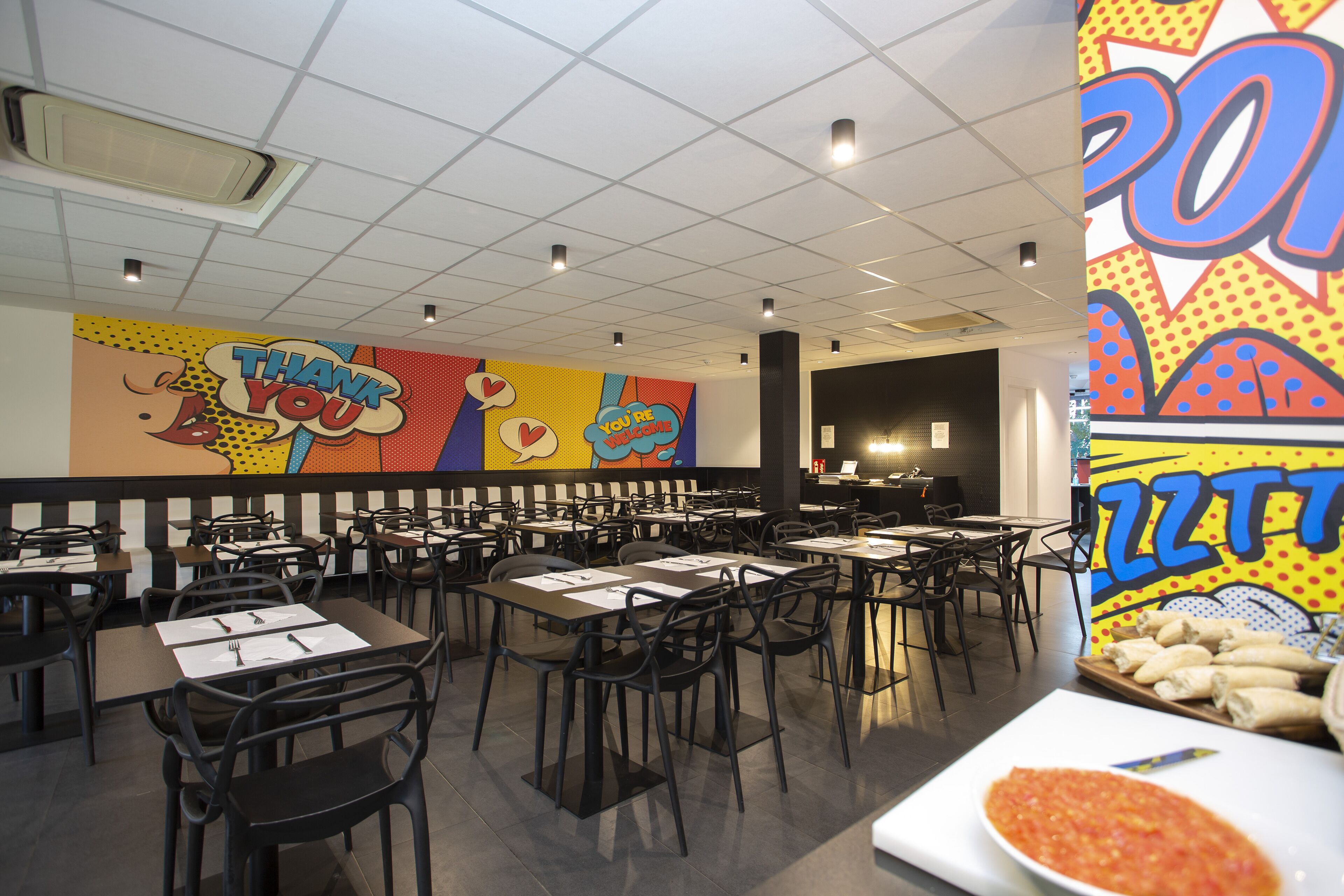 A restaurant with booths and tables, a colorful mural on the wall, and a tray of burritos on a table.