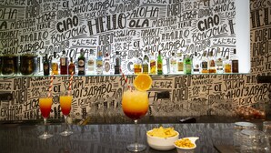 A bar area with a wall covered in multilingual 'Hello' signs, various bottles, and glasses.