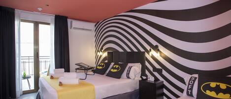 Habitación de hotel con dos camas, vistas al exterior, pared a rayas blancas y negras y una almohada con temática de Batman.