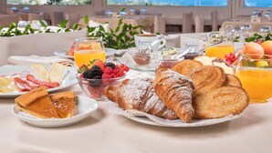 A breakfast setting with croissants, fruit, and beverages on a table with a scenic view. - Hotel Rocce Sarde (Olbia)