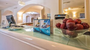 A reception desk with a Panasonic printer, a glass display case with apples, and a brochure titled "myyo experience". - Hotel Rocce Sarde (Olbia)